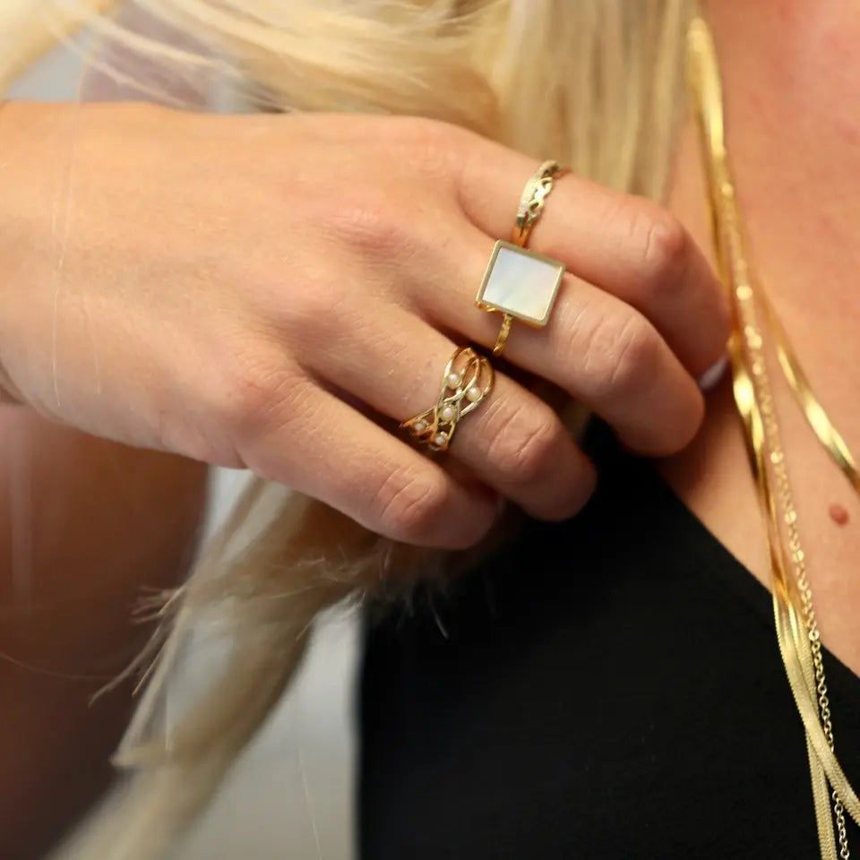Bague en acier inoxydable aux formes ajourées et ornée de petites boules nacrées portée au doigt