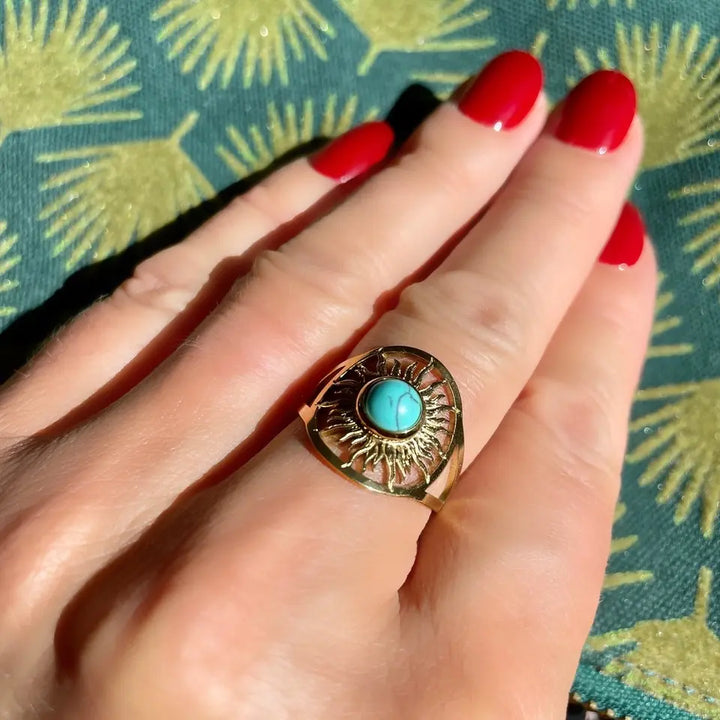 Bague ronde en forme de soleil orné d'une pierre turquoise portée au doigt