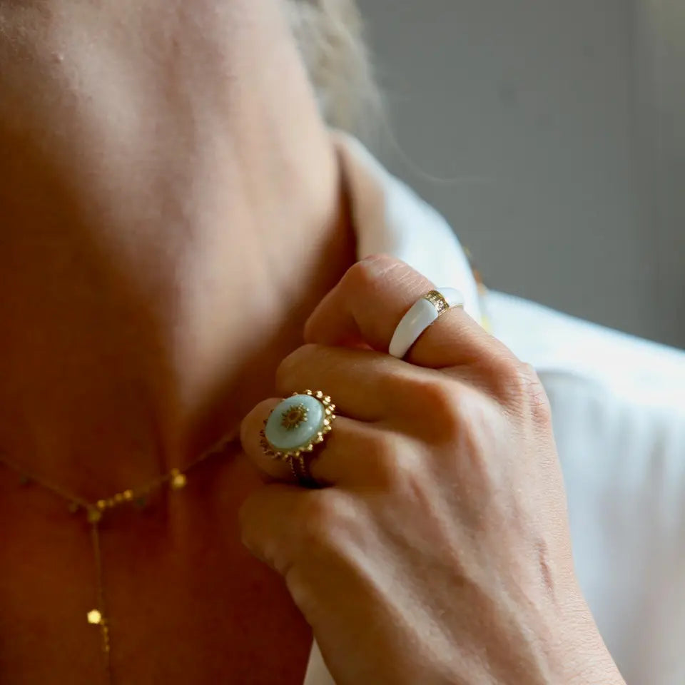 Bague fine en acier inoxydable ornée de strass au centre et d’une finition colorée blanche portée au doigt