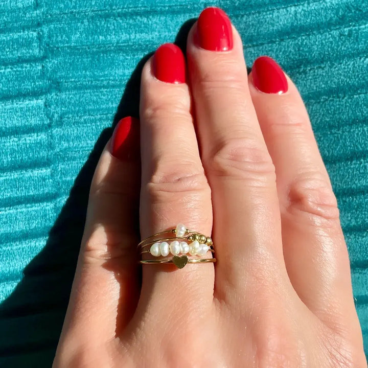 Bague multi rangs en acier inoxydable composée de 4 rangs sertis de perles d’eau douce et d'un cœur portée au doigt