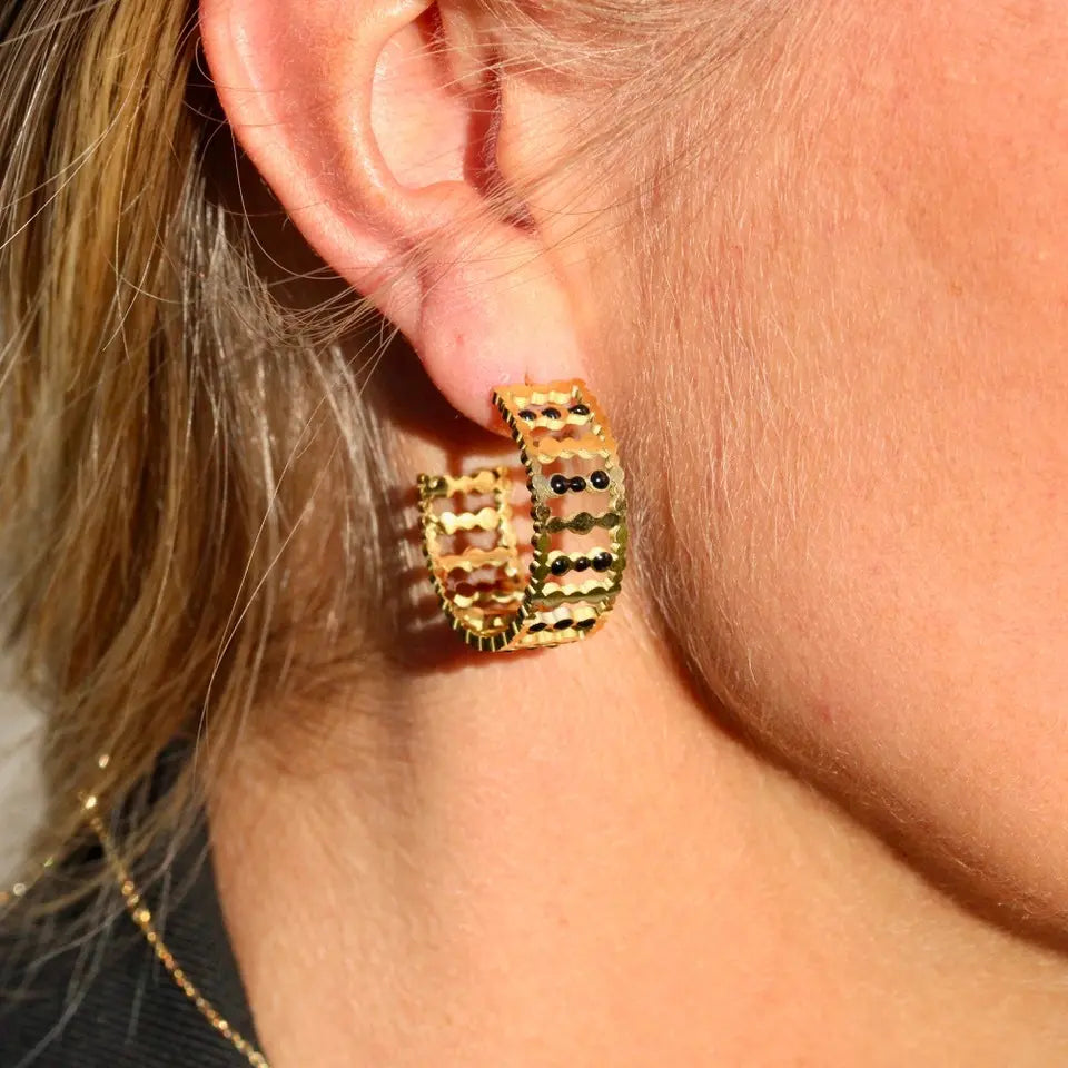 Boucles d’oreilles de type créoles structurées en acier inoxydable doré orné de pointillés noir portées aux oreilles