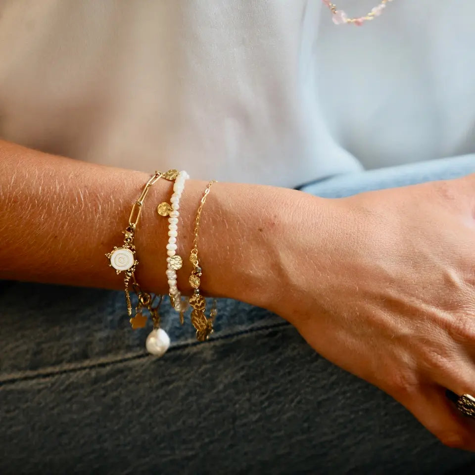 Bracelet CHARMS à maillon en acier inoxydable doré avec pampilles perle d’eau douce, étoile, fleur et soleil porté au poignet en accumulation