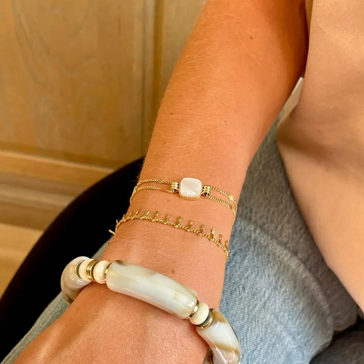 Bracelet double chaine en acier inoxydable doré composé d'un pendentif carré en nacre porté au poignet