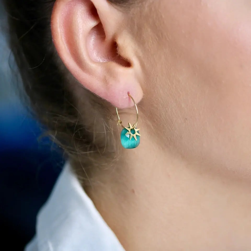 Boucles d’oreilles mini créoles avec pendentifs composées d’une pierre naturelle et d’un motif en forme de soleil doré en acier inoxydable. portées aux oreilles